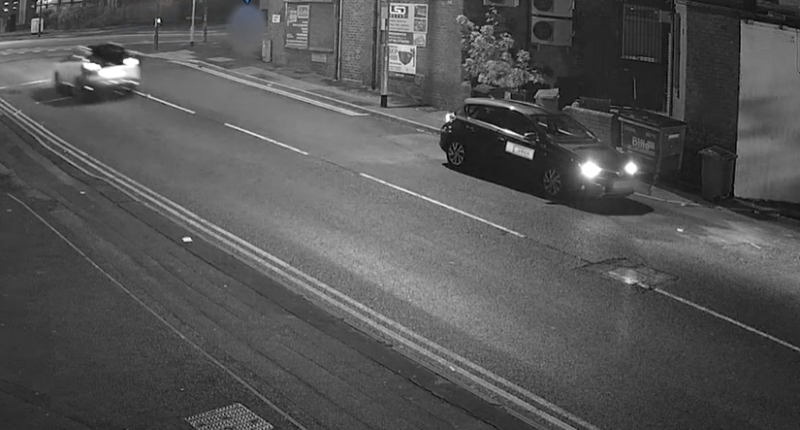 Nighttime security camera footage of a street with two cars.