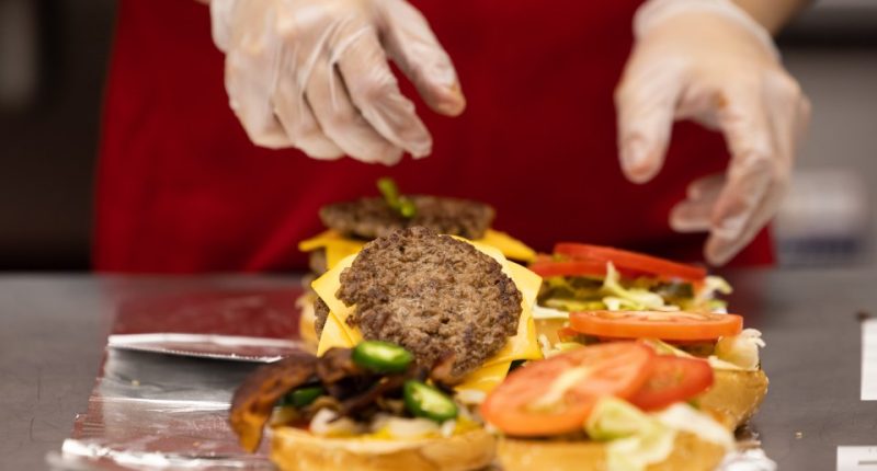 A Five Guys employee assembling burgers.