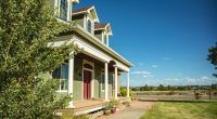 Green house with a large porch and surrounding lawn.