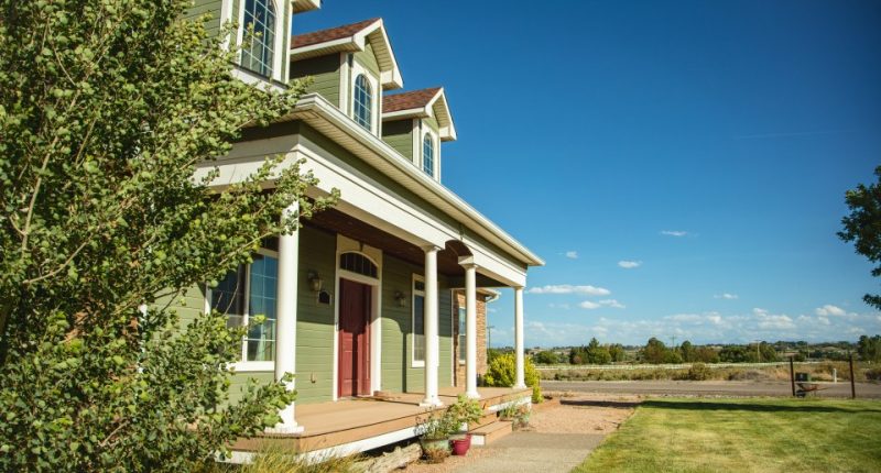 Green house with a large porch and surrounding lawn.