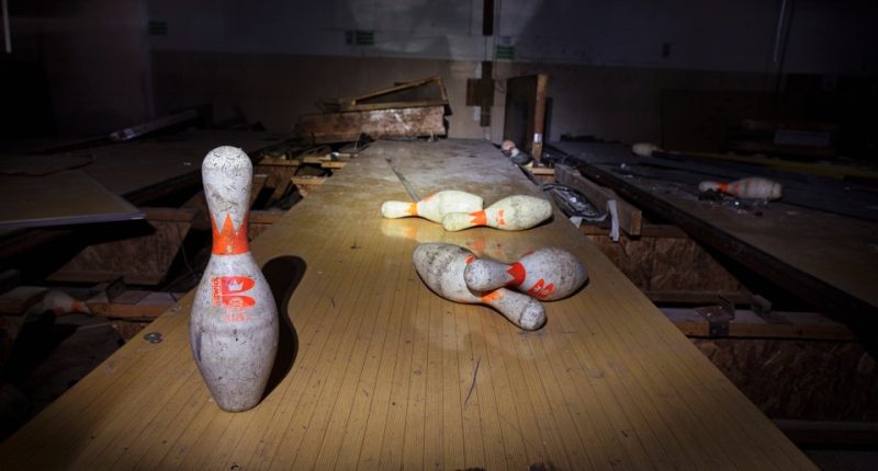 Abandoned bowling alley with several bowling pins on the lane.