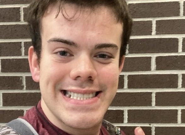 Photo of a young man smiling and giving a peace sign.