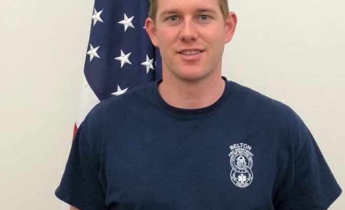Portrait of a firefighter in uniform standing in front of an American flag.