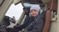 A child sits in a helicopter next to the pilot.