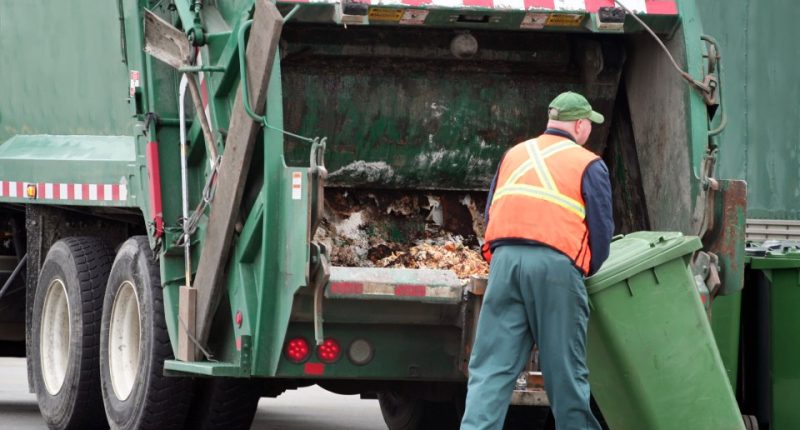 Sanitation worker emptying a green bin into a garbage truck.