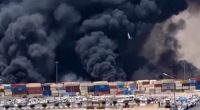 Large plume of black smoke billowing over a port.