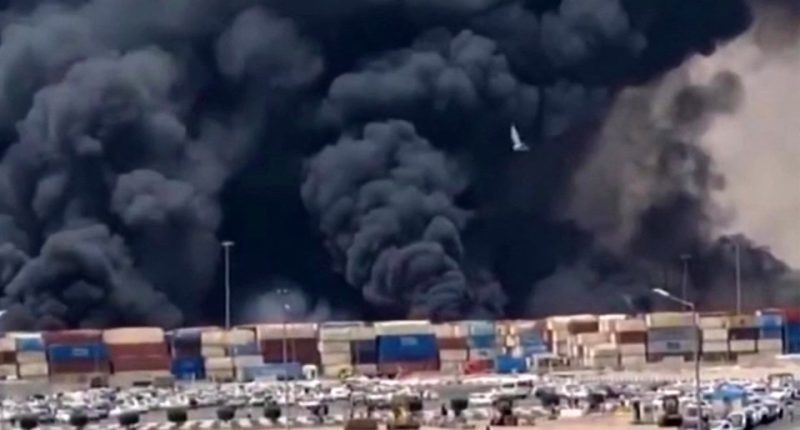 Large plume of black smoke billowing over a port.