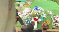 Pallbearers lowering a coffin into a grave at a funeral.