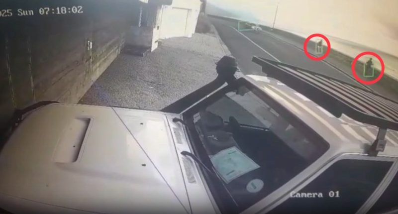 Security camera footage of a vehicle with two people visible in the distance.