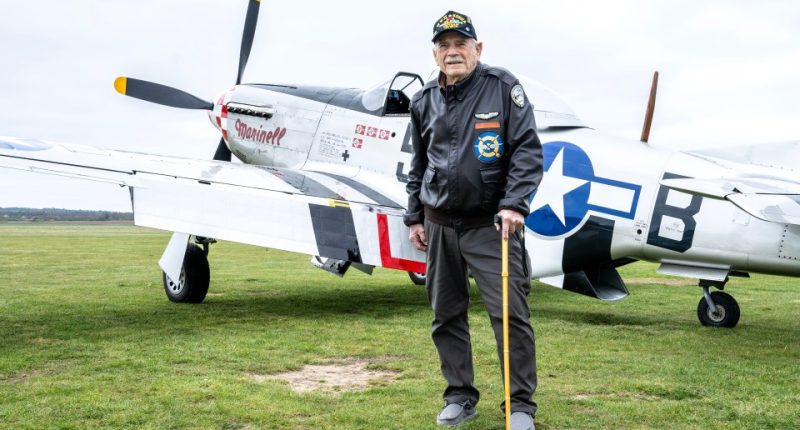 WWII veteran standing in front of a fighter plane.