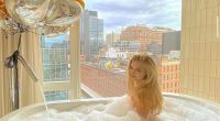 Woman in a bubble bath in front of a window with a city view and balloons.