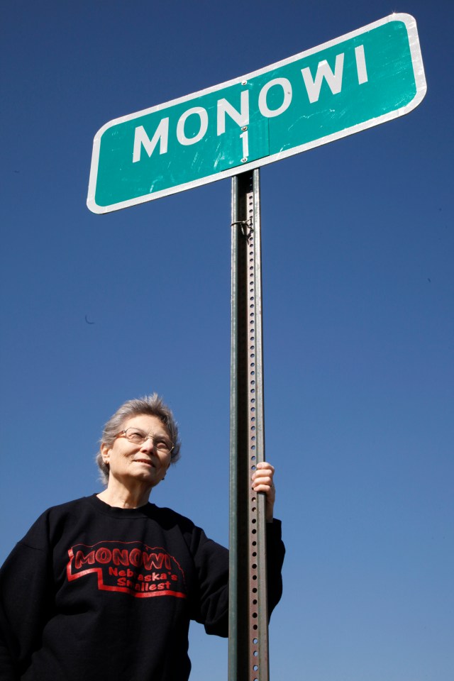 Woman standing by Monowi, Nebraska town sign.