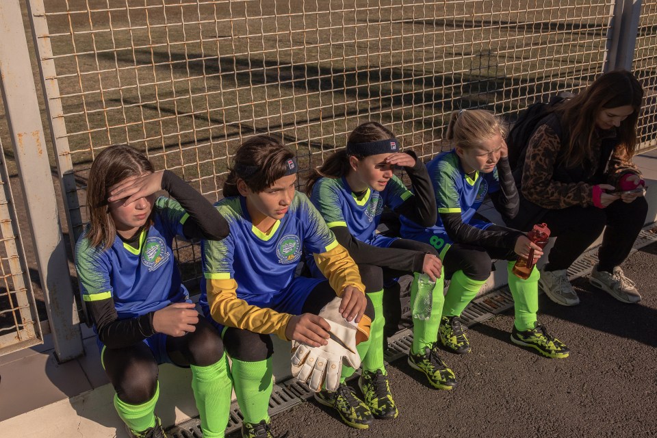 Girls' soccer team from Kherson, Ukraine, sitting near a fence before a match.
