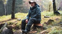 Man sitting on a tree stump in a forest.