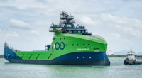 Large green and blue ship being towed by a smaller tugboat.