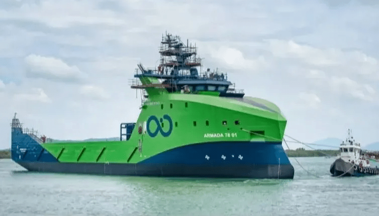 Large green and blue ship being towed by a smaller tugboat.