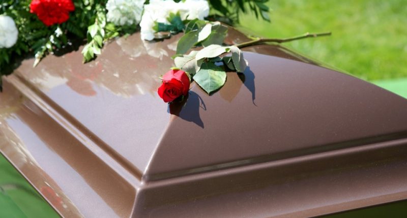 A single red rose on a brown casket.