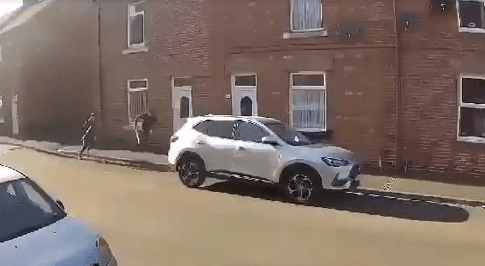 Two people running past a parked silver SUV on a residential street.