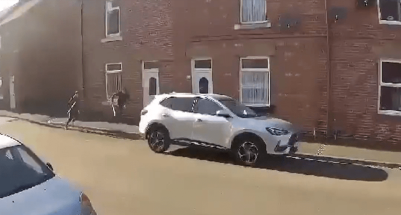 Two people running past a parked silver SUV on a residential street.