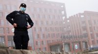 Security guard in face mask standing in front of the Wuhan Institute of Virology.