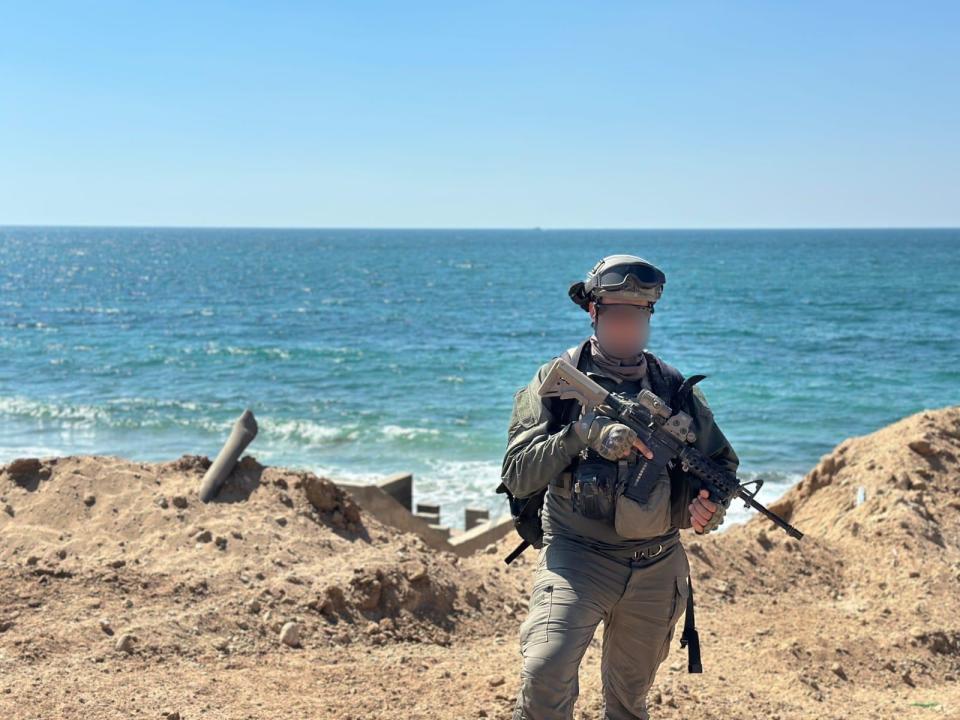 IDF reservist Captain U standing by the ocean with a rifle.