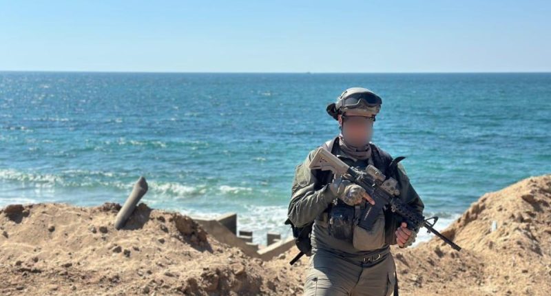 IDF reservist Captain U standing by the ocean with a rifle.