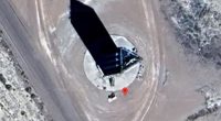 Aerial view of a tall, dark, obelisk-shaped structure in a desert landscape.