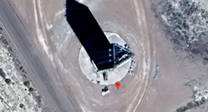 Aerial view of a tall, dark, obelisk-shaped structure in a desert landscape.