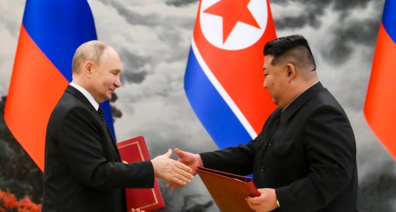 Vladimir Putin and Kim Jong Un shaking hands at a signing ceremony.