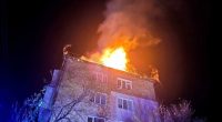Fire engulfing the roof of a building at night.