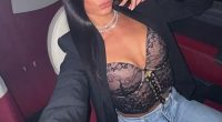 Woman in a car, wearing a black blazer and lacy top.