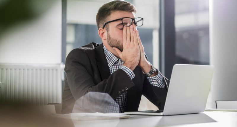 Businessman at desk with laptop, looking stressed.