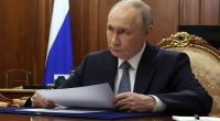 Vladimir Putin reviewing documents at a meeting.