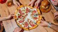 High-angle view of six young people sharing a pizza and a burger in a pub.