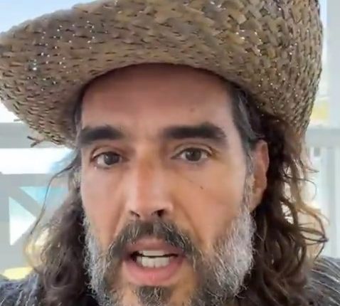 Close-up of a man with long hair and a beard wearing a straw hat, speaking.