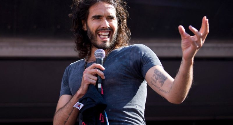 Russell Brand speaking into a microphone at a rally.