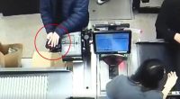 Surveillance footage of a person installing a card skimmer at a grocery store checkout.