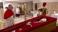 A cardinal and a Swiss Guard stand near an open casket containing the deceased Pope Benedict XVI.
