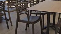 Outdoor restaurant patio with tables and chairs, overlooking a beach and city.