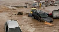Flooded harbor in Naoussa, Paros, Greece, with several submerged vehicles.