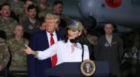 Gretchen Whitmer speaking at a podium with Donald Trump in the background.