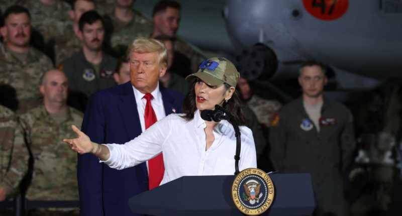 Gretchen Whitmer speaking at a podium with Donald Trump in the background.