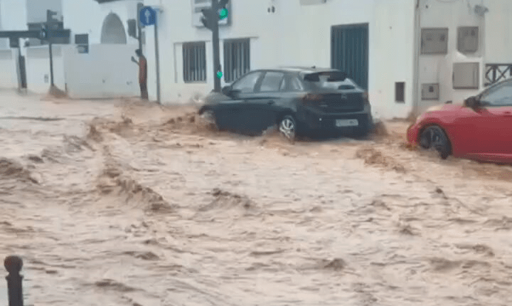 Flooded street with cars partially submerged.