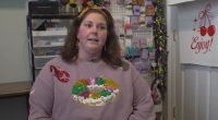 A woman wearing a Mardi Gras-themed sweatshirt discusses issues with the USPS.