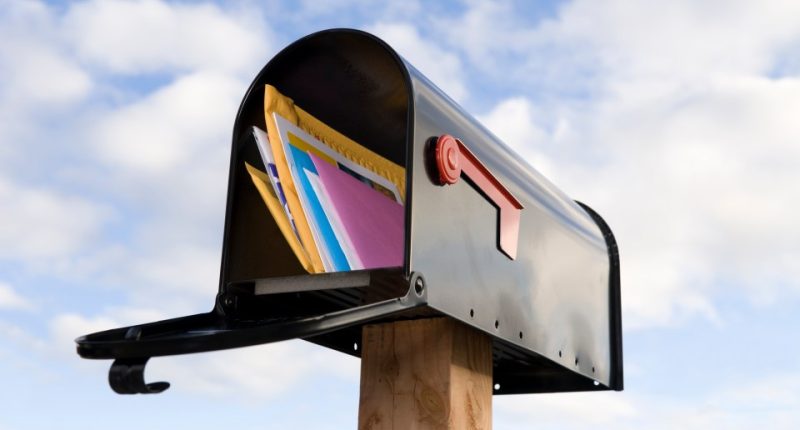 Full mailbox with letters under a cloudy sky.
