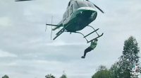 Man clinging to the landing gear of a helicopter in flight.