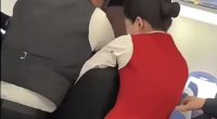 Flight attendants and passengers restraining two fighting female passengers.