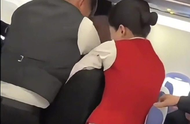 Flight attendants and passengers restraining two fighting female passengers.