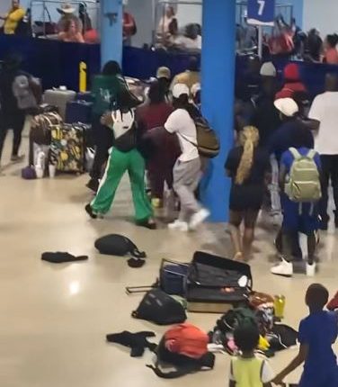 A large group of people fighting and scattering luggage in a terminal.