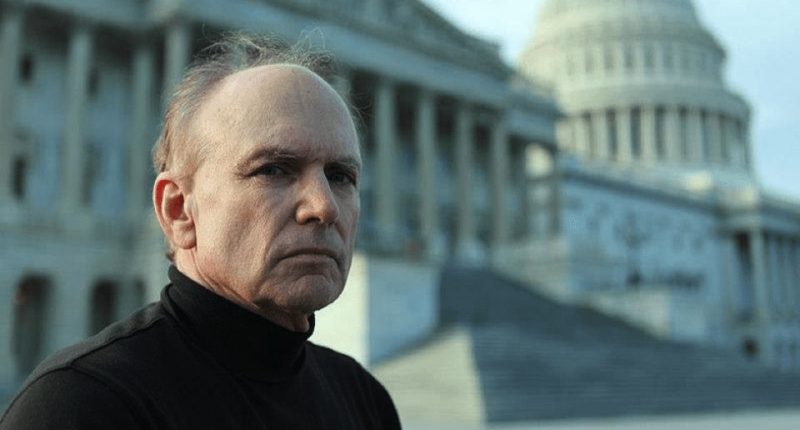 a bald man stands in front of the capitol building